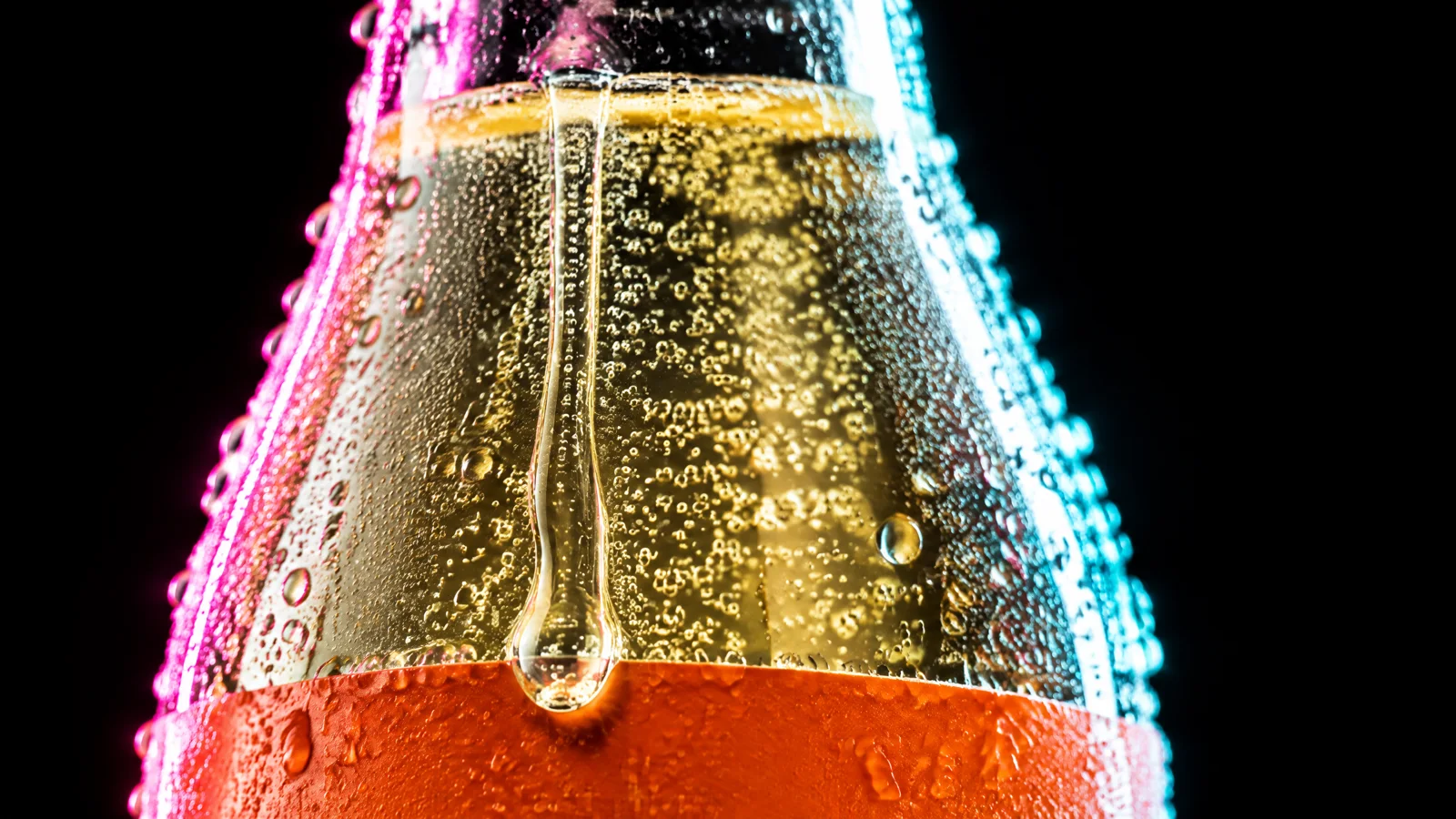 The macro still: the bottle's shoulder covered in condensation, one large drop running over the top edge of the orange band