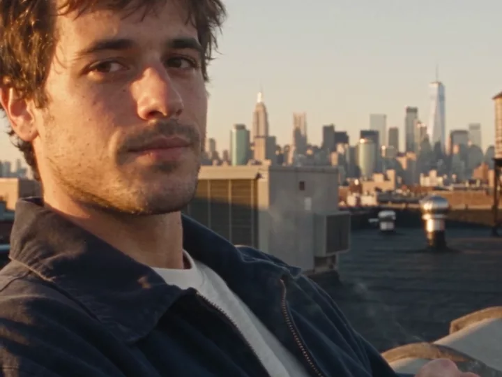 A close-up of the man on the rooftop with the Manhattan skyline behind him, including One World Trade Center