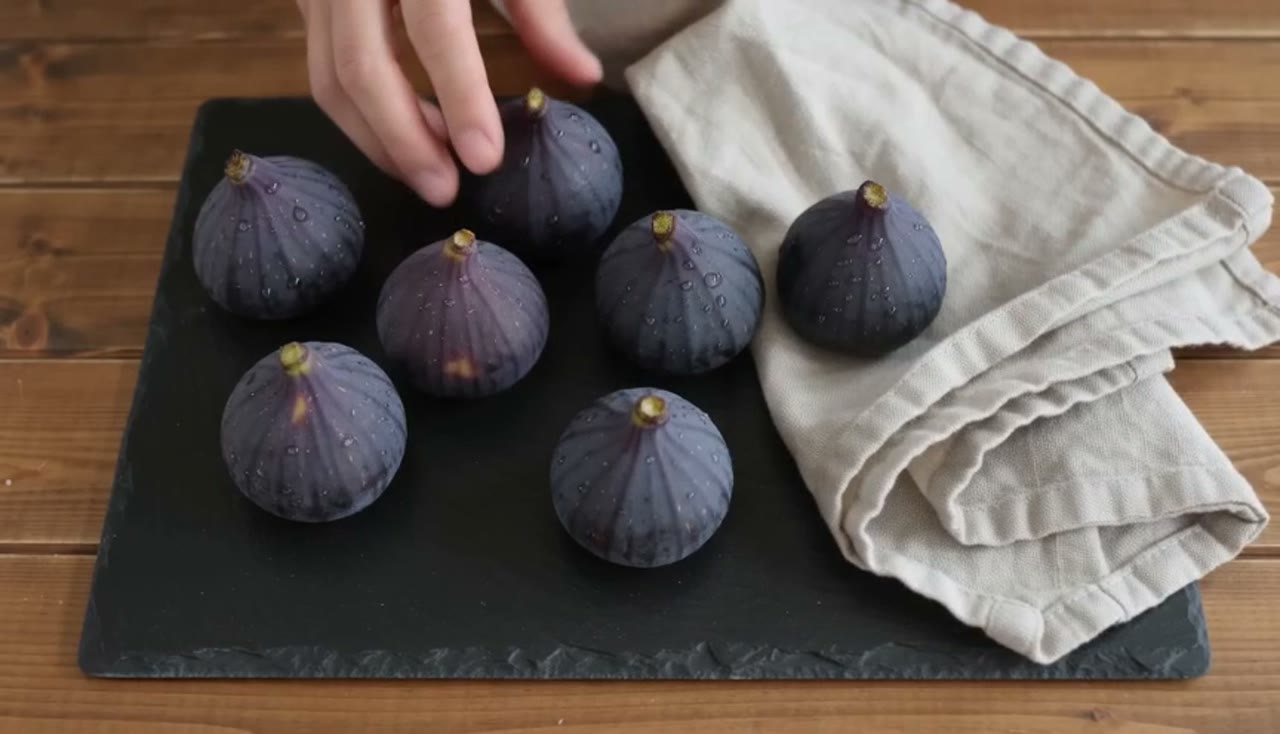 Seedance 2.0 Fast로 만든 예시: Overhead: two hands arrange ripe figs and a linen cloth on a slate board, then a quick rack focus to a knife splitting one open, the flesh…